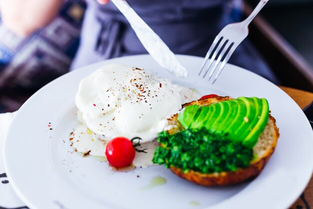 The girl holds a knife and a fork and starts to eat her breakfast