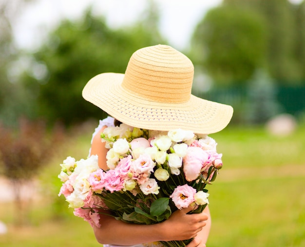 The girl holds a large bouquet of pink and white peonies in front of her.