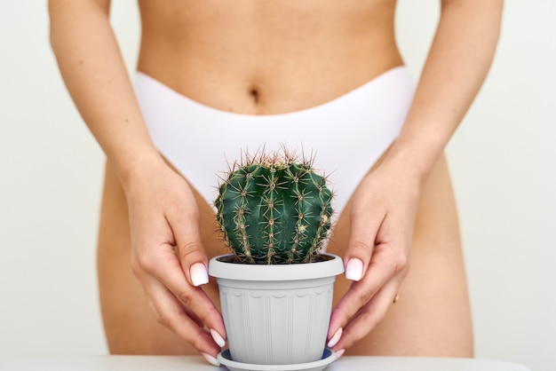 The girl holds a large cactus in the groin or bikini area. The concept of intimate hygiene, epilation and depilation, deep bikini shaving.