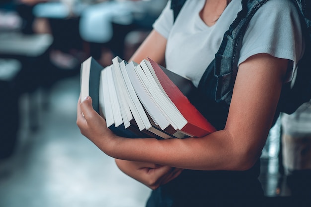 The girl holds many books and in the library.