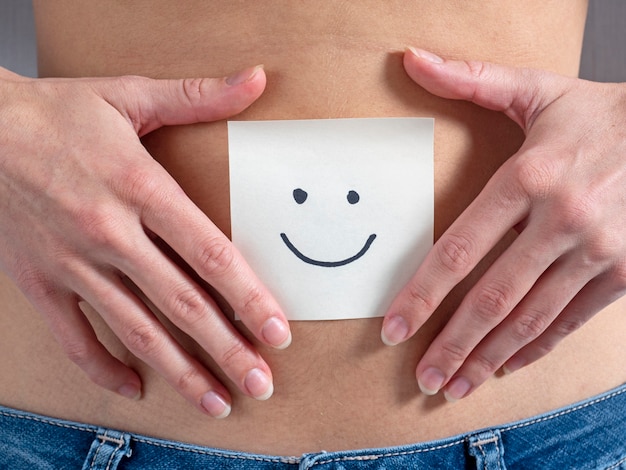 The girl holds a paper sticker with a smiley face in front of her bare stomach. Concept of pregnancy and motherhood