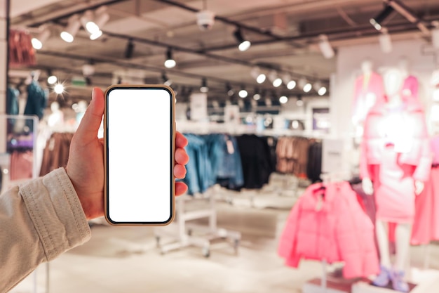 Photo a girl holds a phone in her hand with a blank isolated screen on the background of a blurred shopping center