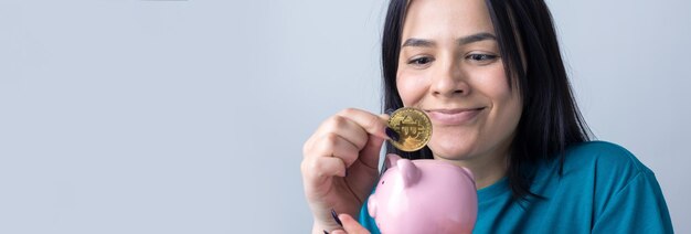 The girl holds a pink piggy bank and a coin in her hands. The concept of wealth and accumulation.