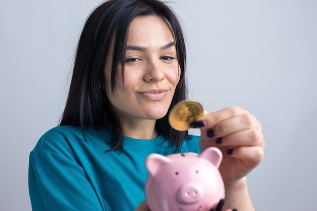 Девушка держит розовую копилку и монету в руках. Понятие богатства и накопления.