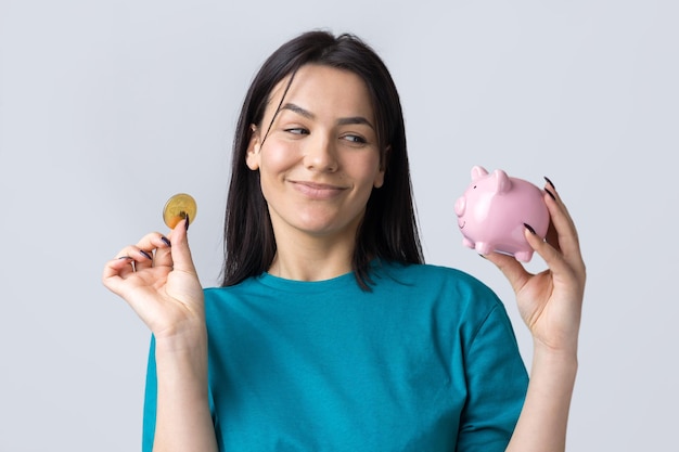 The girl holds a pink piggy bank and a coin in her hands. The concept of wealth and accumulation.