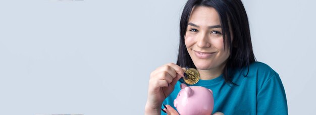 The girl holds a pink piggy bank and a coin in her hands. The concept of wealth and accumulation.