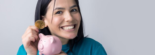 The girl holds a pink piggy bank and a coin in her hands. The concept of wealth and accumulation.