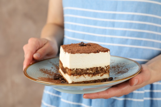 Girl holds plate with delicious tiramisu against brown