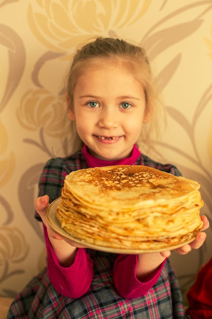 A girl holds a plate with a stack of pancakes