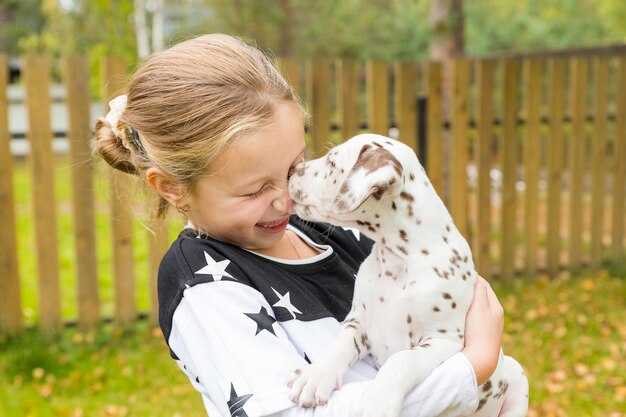 女の子は彼女の腕に子犬を保持しますダルメシアンの子犬を抱き締めるかわいい女の子ブロンドの髪の少女