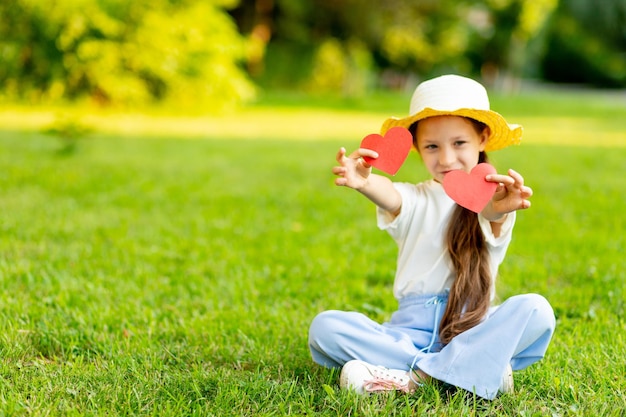 A girl holds red hearts in focus on a green lawn in summer the concept of Valentine's day