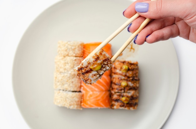 girl holds a roll with chopsticks.