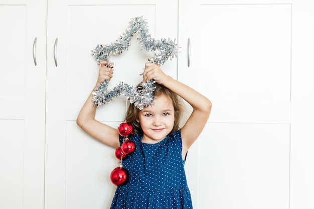 女の子は新年とクリスマスのために家を飾るために彼女の手に星を持っています、子供は休日の準備をしていて、両親を助けて、贈り物を待っています