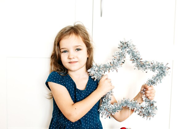 A girl holds a star in her hands to decorate the house for the new year and Christmas, the child is preparing for the holiday, helping parents, waiting for gifts