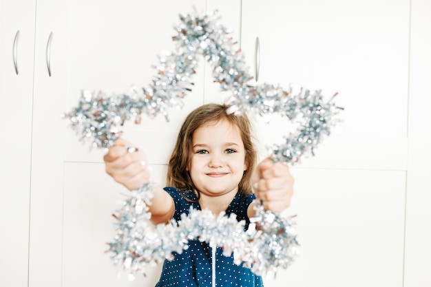 女の子は新年とクリスマスのために家を飾るために彼女の手に星を持っています、子供は休日の準備をしていて、両親を助けて、贈り物を待っています