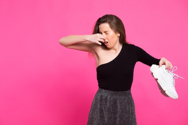 Girl holds stinky sneakers and closes her hand with her nose\
smell of shoes