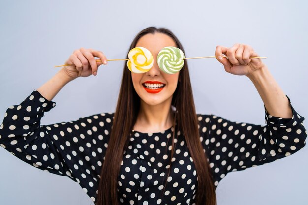 Girl holds two lollipops near eyes cheerful lady in dotted\
shirt over white background