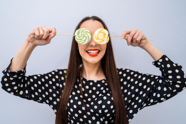 Photo girl holds two lollipops near eyes. cheerful lady in dotted shirt over white background.