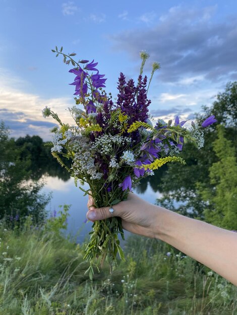 The girl holds wild flowers in her hand overlooking the lake and the sky