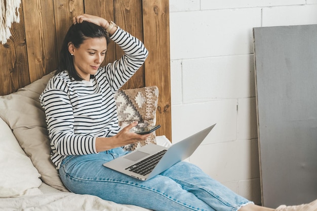 Photo girl at home on her bed uses laptop and phone