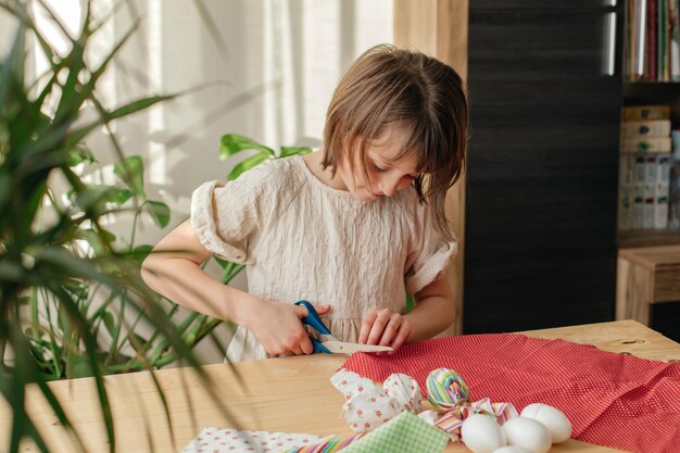 家にいる女の子が耳のあるウサギの形をしたイースターの織物卵を作るための布を準備している