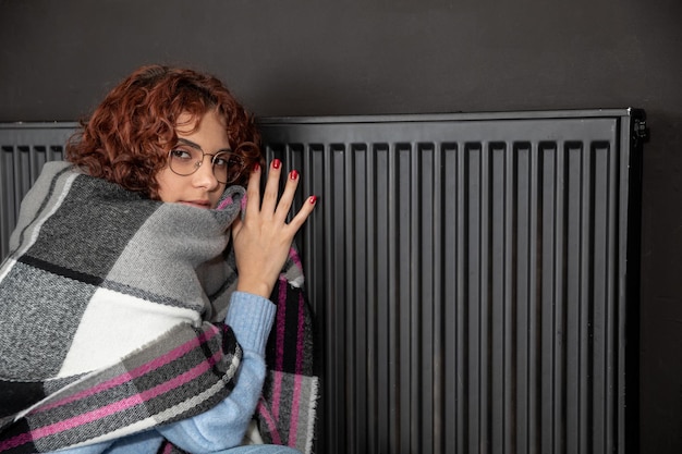 Photo a girl huddled around a hot radiator the first start of the central heating system