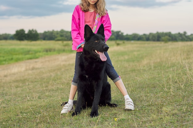 Girl hugging big black dog shepherd, child and pet walking in nature