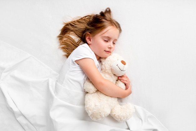 Девушка обнимает плюшевого мишку на кровати
