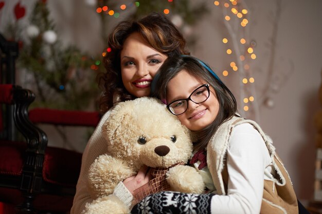 Girl hugging teddy enjoying Christmas eve with mother.