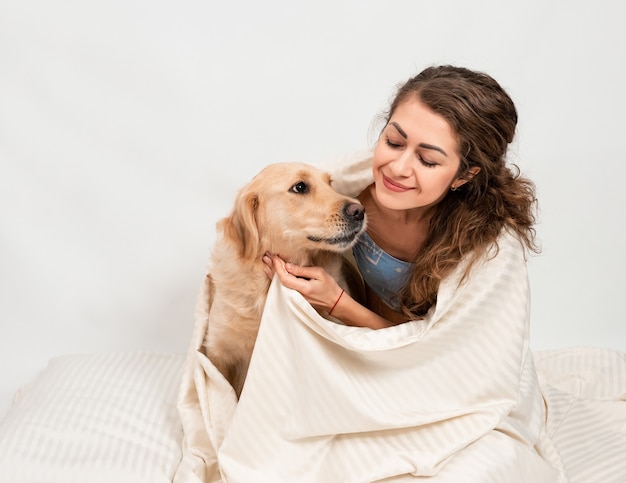 girl hugging with her labrador retriever dog wrapped n a white blanket.