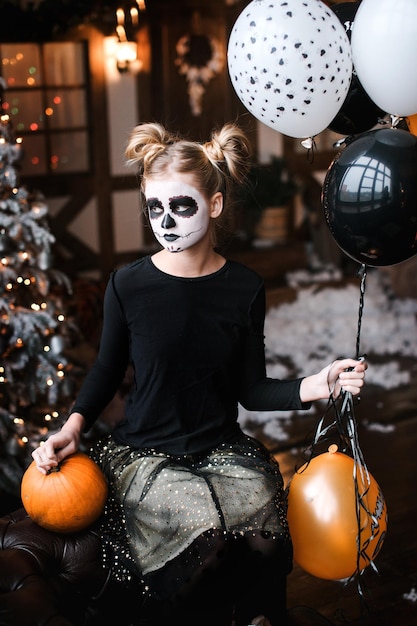 A girl in the image of a little witch holds a ball in the form of a pumpkin