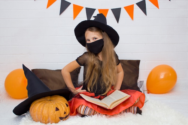 Фото Девушка в черной маске и в костюме ведьмы с книгой чародея сидит улыбаясь, глядя в камеру