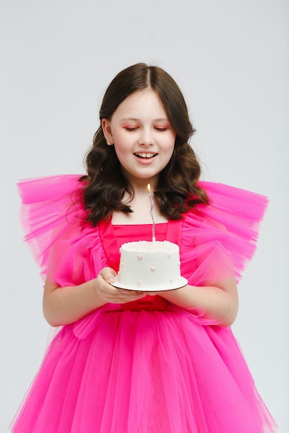 사진 분홍색 드레스를 입은 소녀가 흰색 배경에 있는 케이크에 촛불을 불고 있습니다.