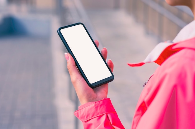 Фото Девушка в розовой куртке держит в руках макет смартфона с белым экраном.