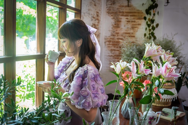 사진 공주 드레스를 입은 소녀는 식물, 꽃, 불과 같은 창문에서 차를 마시고 있습니다.