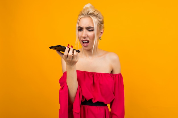 Девушка в красном платье с негодованием говорит по телефону на желтом пространстве студии