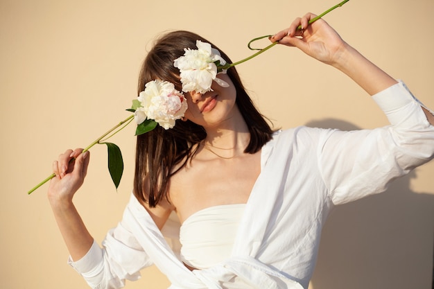 写真 白いシャツを着た女の子は、ベージュの背景に牡丹の花で目を閉じます