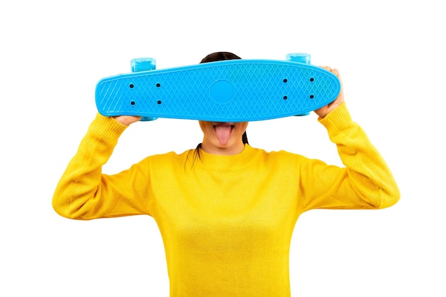 写真 黄色いプルオーバーを着た女の子が青いスケートボードで顔を覆い、見る人に舌を見せている