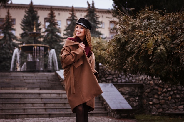 Фото Девушка в коричневом пальто падает в город, улыбаясь