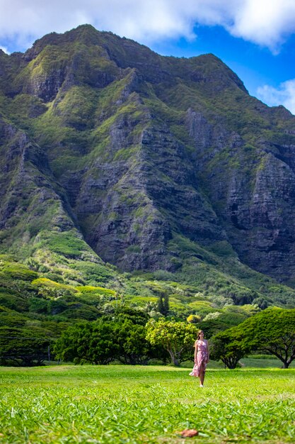 Фото Девушка в длинном платье ходит по траве в куалоа-пойнт на оаху, гавайи, с видом на могучую зеленую гору