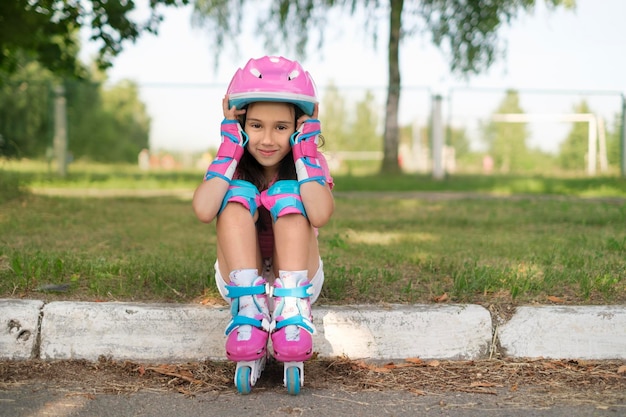 Фото Девушка в розовом шлеме и роликовых коньках сидит на обочине тротуара