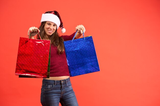주황색 배경에 크리스마스 쇼핑백을 들고 웃고 있는 산타클로스 모자를 쓴 소녀