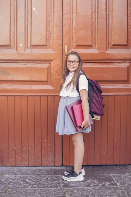 Фото Девушка в школьной форме с рюкзаком перед большими дверями