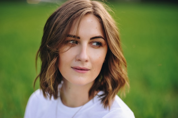 The girl is blonde, brown hair, in a white shirt and blue midi skirt. Walking in the field, through the green grass. Portrait of a girl. Positive and smile.