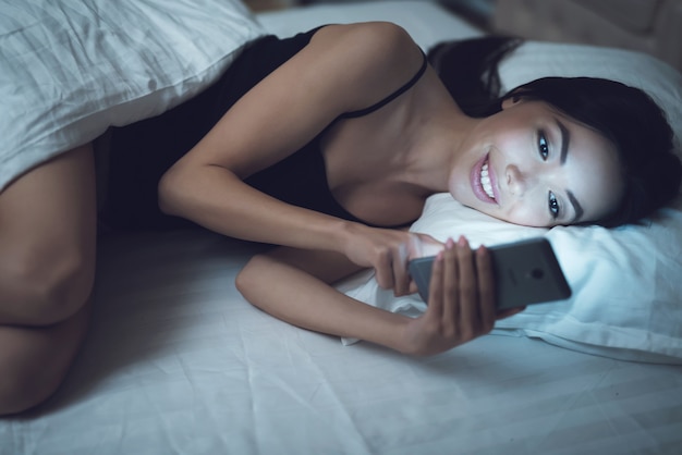 Girl is in a dark room in bed looks at the smartphone.