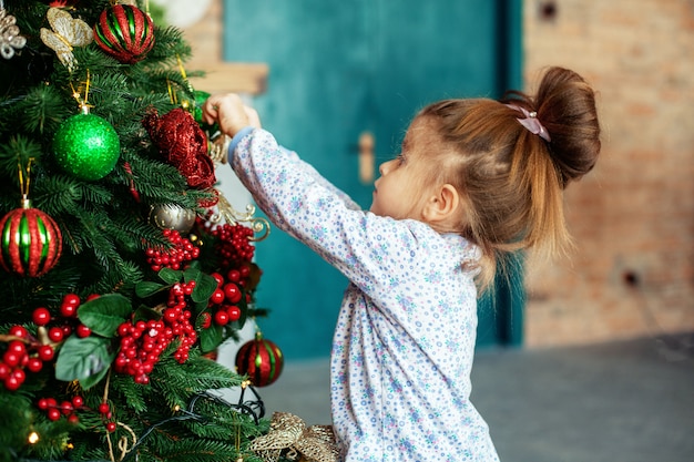 A girl is decorating a Christmas tree in the house. The concept of a Merry Christmas, holiday, family.