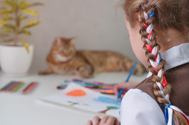 A girl is drawing a drawing and a cat is lying on the table