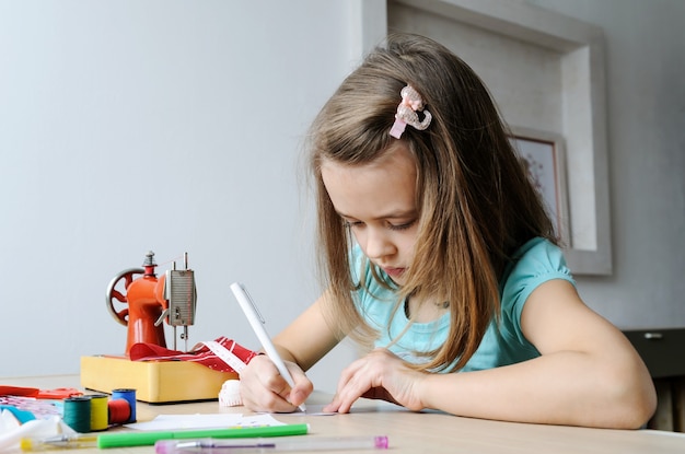 The girl is drawing a sketch of a dress for a doll