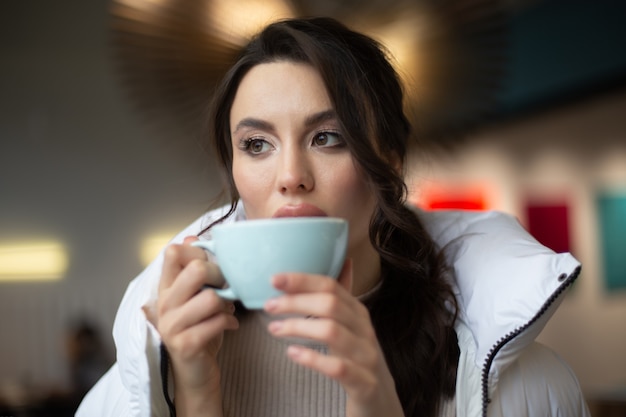 女の子はカフェで温かい飲み物を飲んでいます