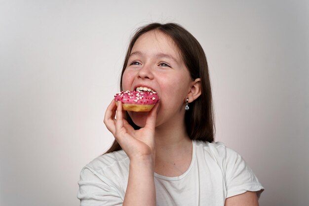 A girl is eating a donut with pink sprinkles on it.